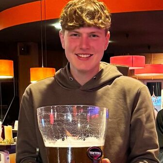 Junge Person in Bowlinghalle hält einen halb gefüllten Biertower und lächelt in die Kamera.